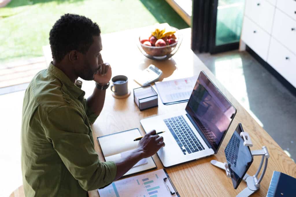 Remote worker, working remotely at desk at home with laptop, and notebook