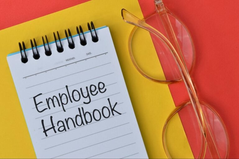 Notebook labeled "Employee Handbook" next to eyeglasses on a colorful background