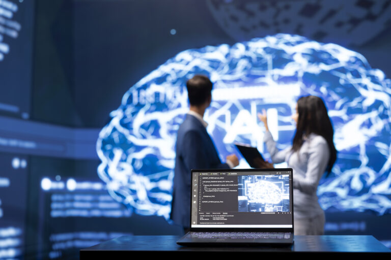 Focus on laptop in workplace used by AI researchers working with artificial intelligence in blurry background. Close up of notebook used by workers developing AI systems in tech startup