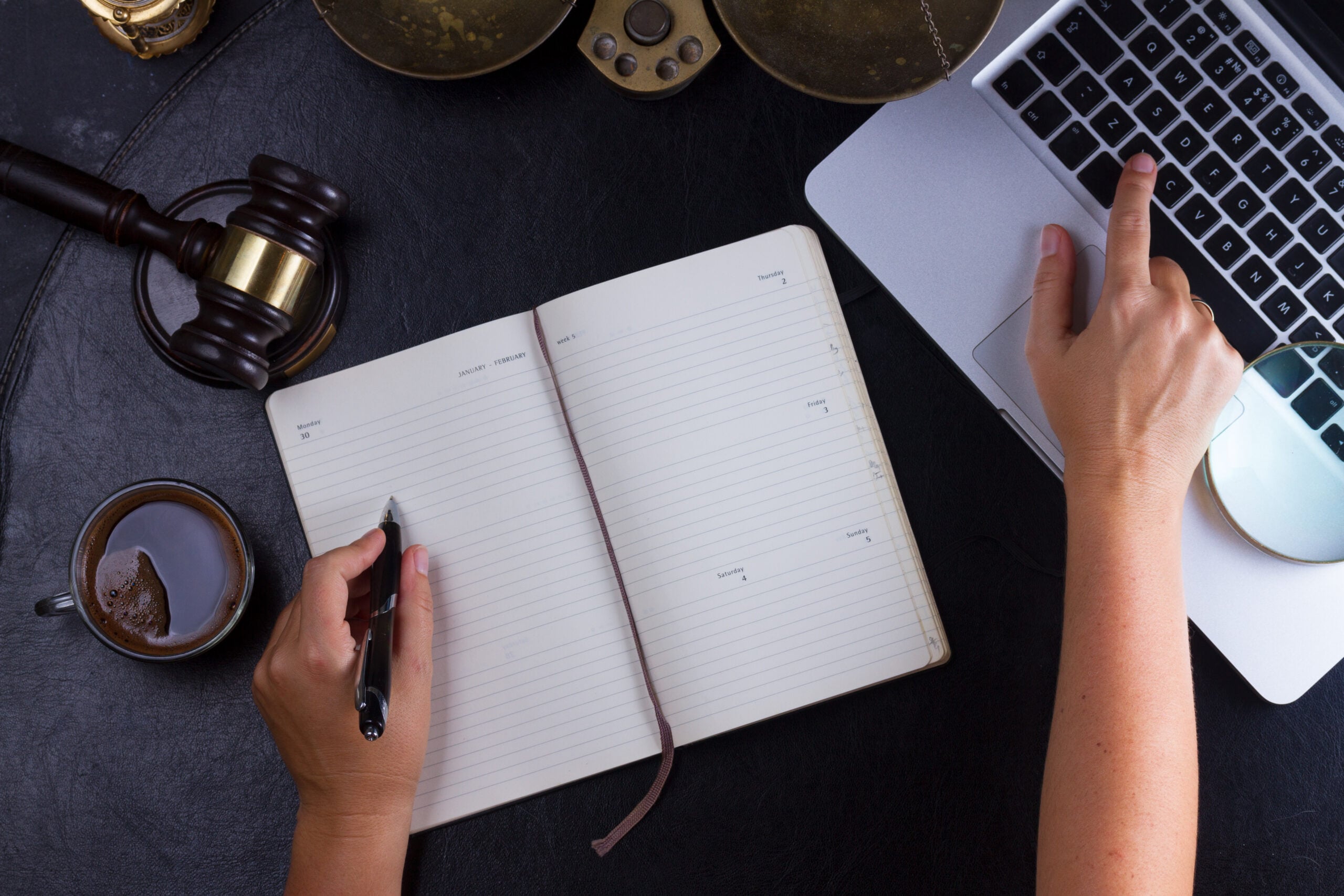 Professional workspace with legal gavel and scales beside a laptop and notebook as a person writes notes during legal research