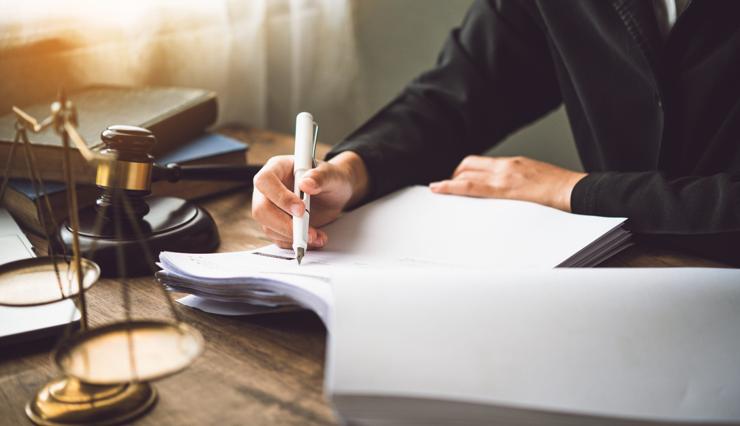 Attorney reviewing and signing legal documents at desk with gavel and scales of justice