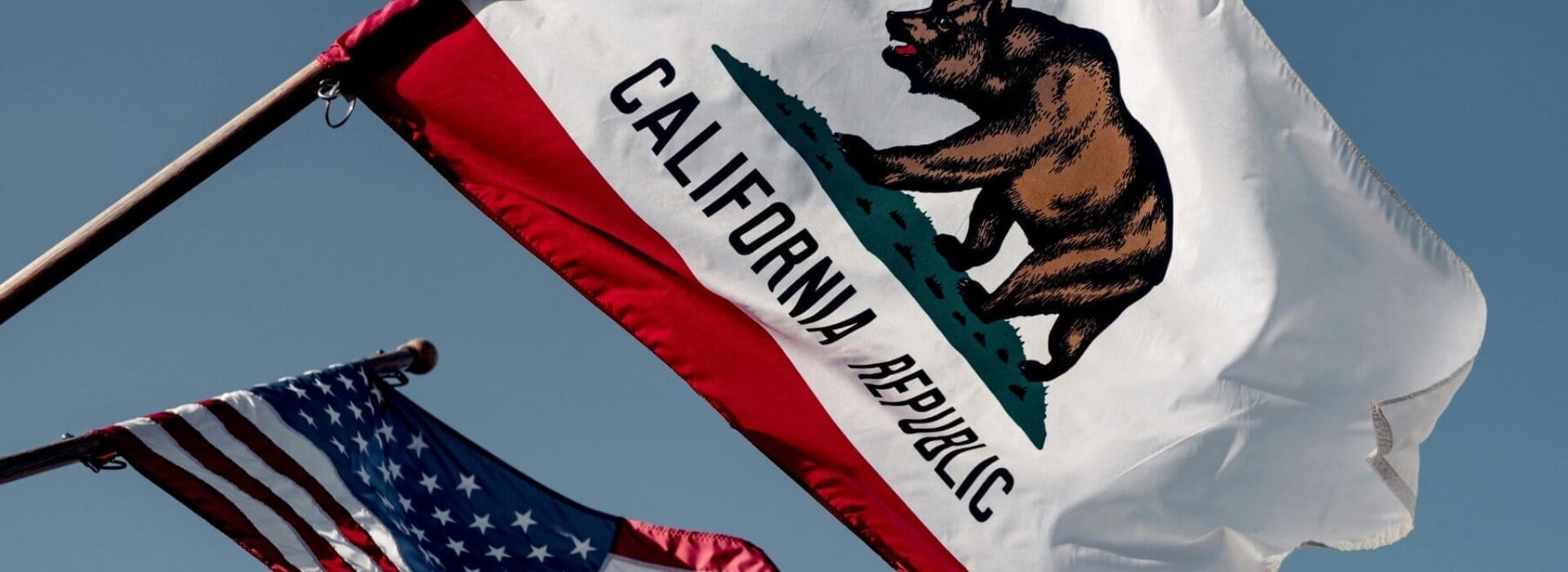 California and American flag waving against a blue sky background